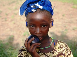Dansa village – A young girl shows an eggplant from the vegetable garden © Sarah Paule Dalle, USC Canada