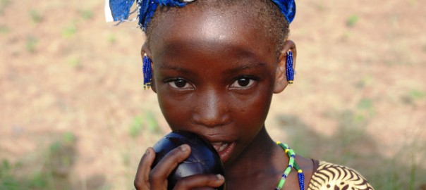 Dansa village – A young girl shows an eggplant from the vegetable garden © Sarah Paule Dalle, USC Canada