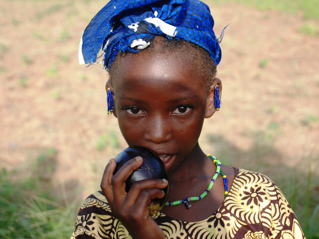 Dansa village – A young girl shows an eggplant from the vegetable garden © Sarah Paule Dalle, USC Canada